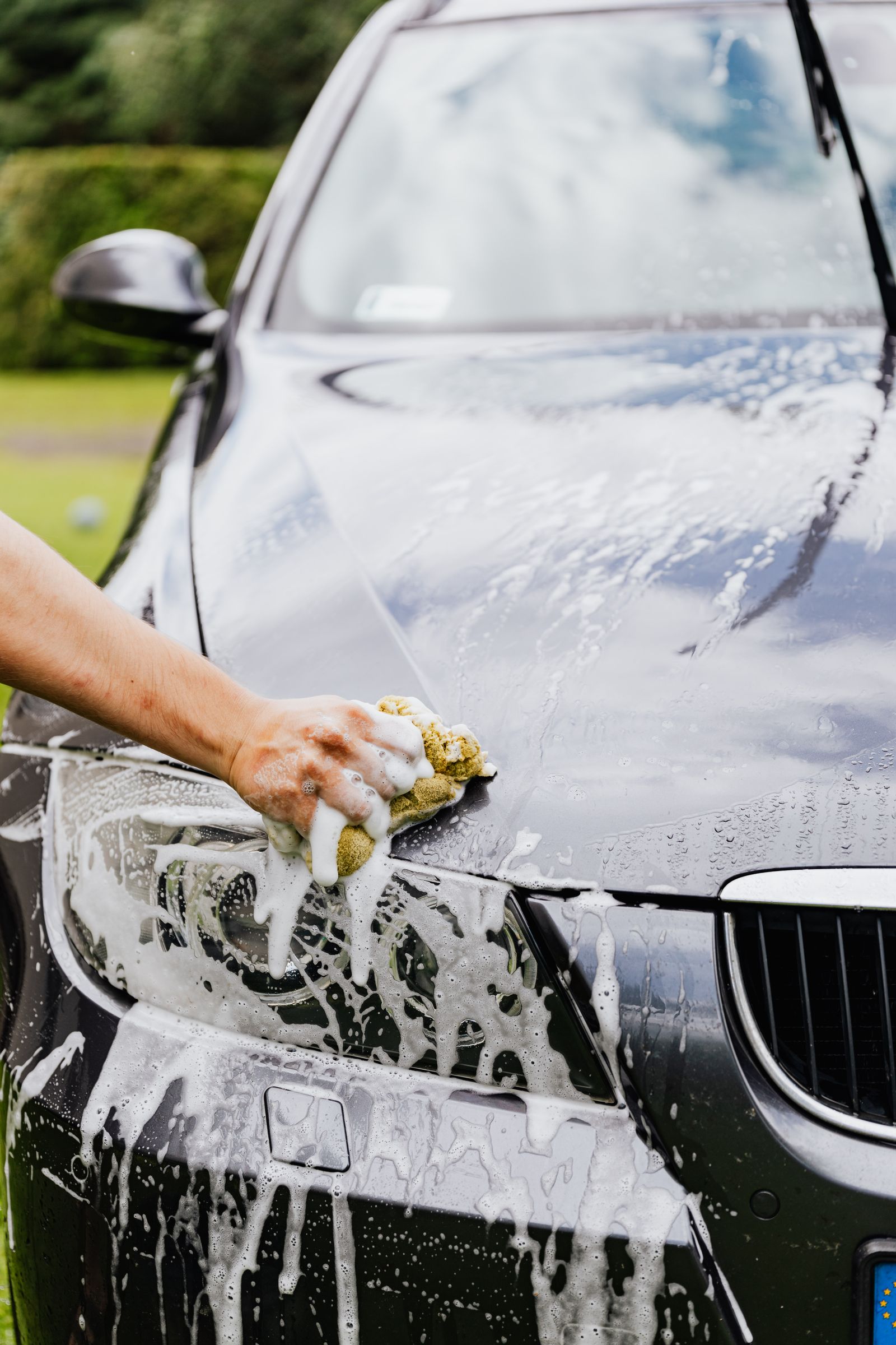 Detailer scrubbing a car headlight with a soapy sponge