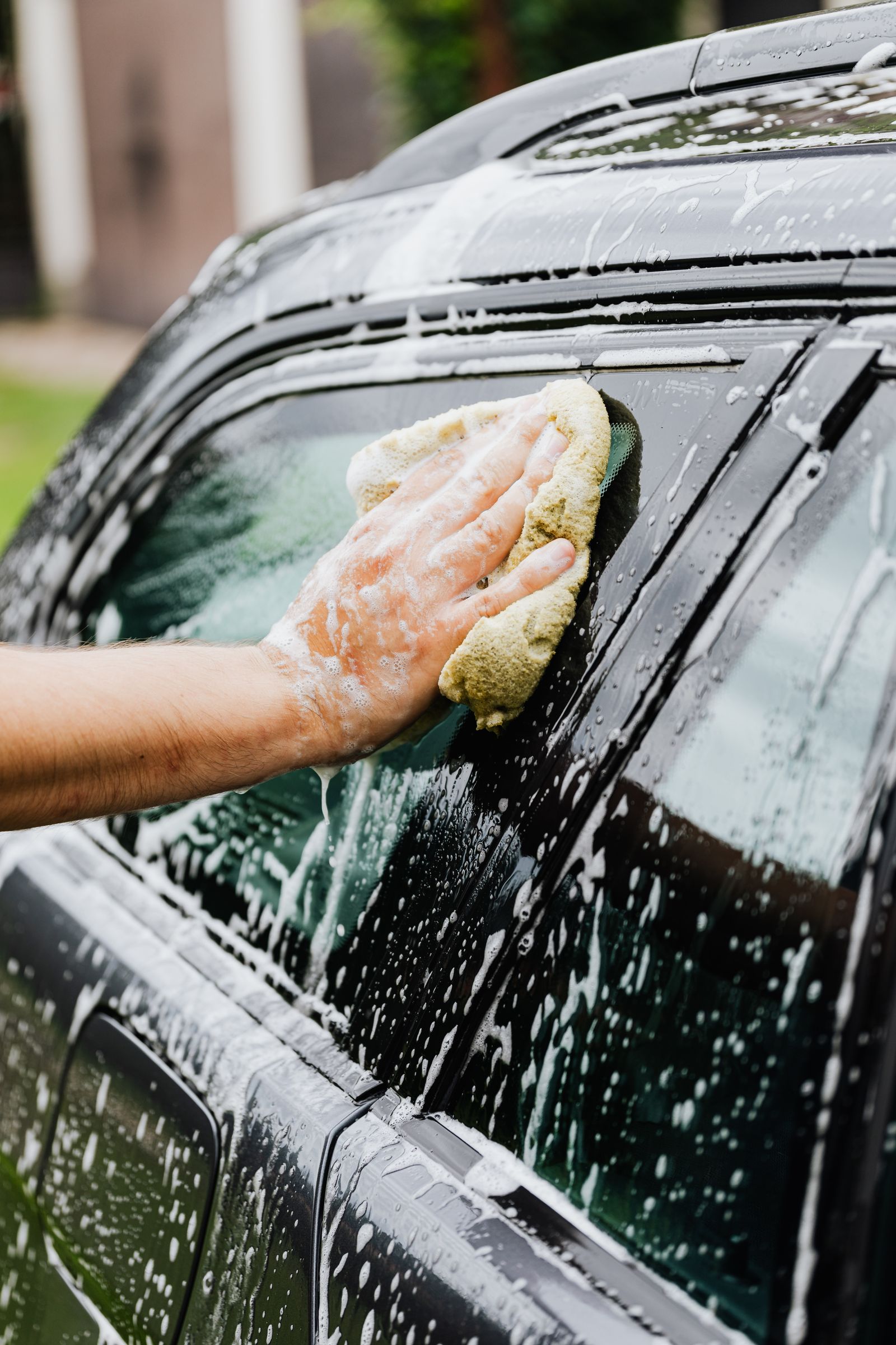 Detailer washing a car window with a soapy sponge in a driveway