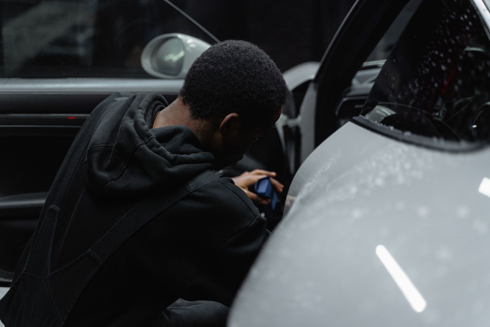 A person is meticulously detailing a luxury car interior under dim lighting, highlighting precision and care.