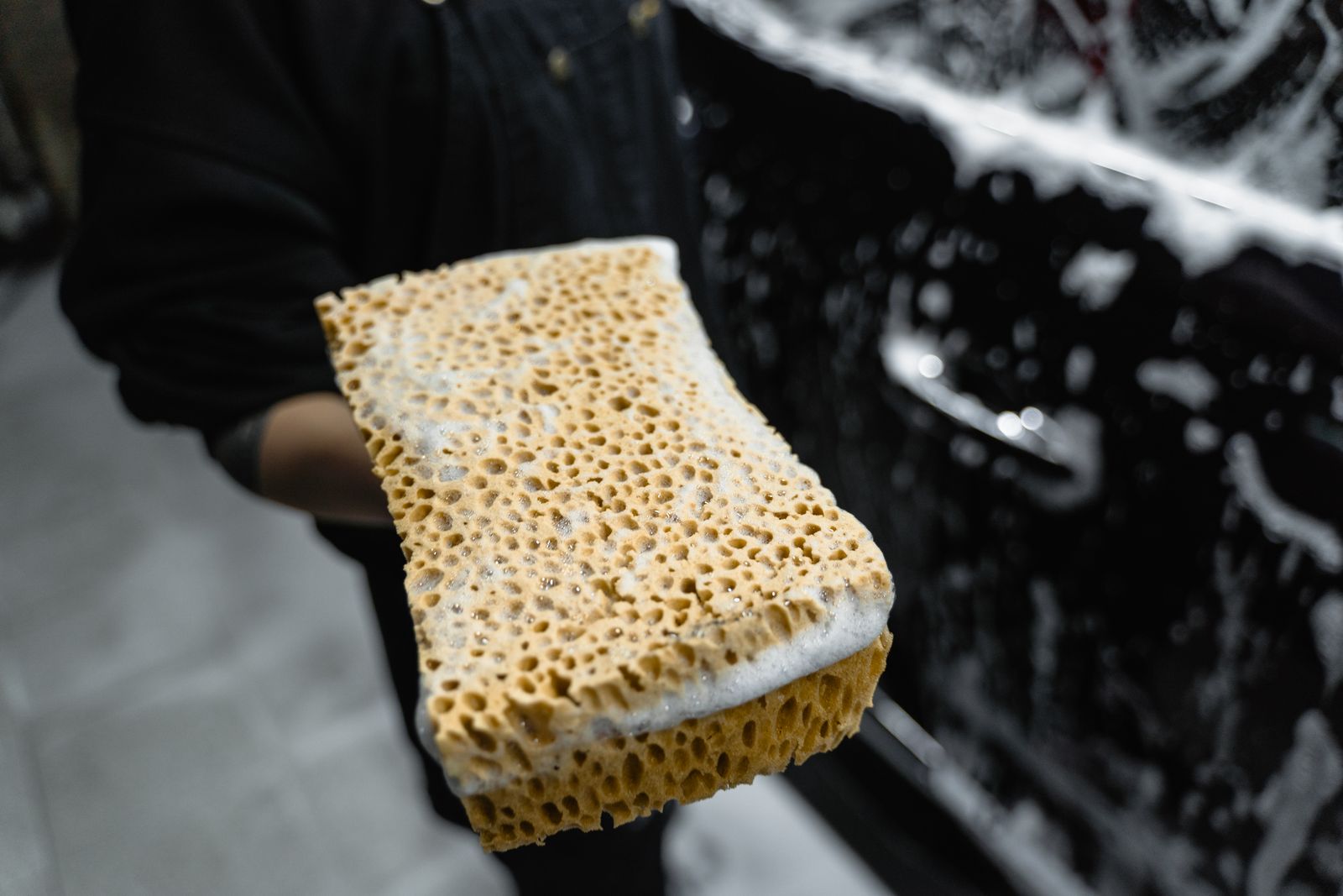 Detailer holding a soapy sponge beside a car