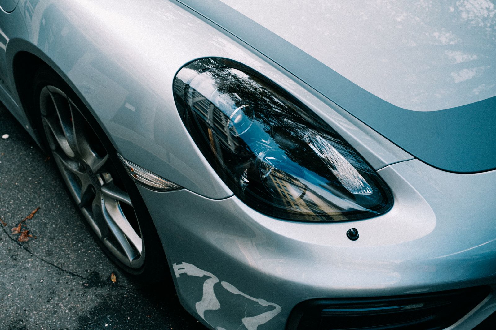 Detailed close-up of a parked silver car showcasing its shiny reflective headlight and modern design.